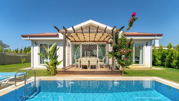 Una casa moderna con piscina, un patio con mobiliario exterior y una pérgola.