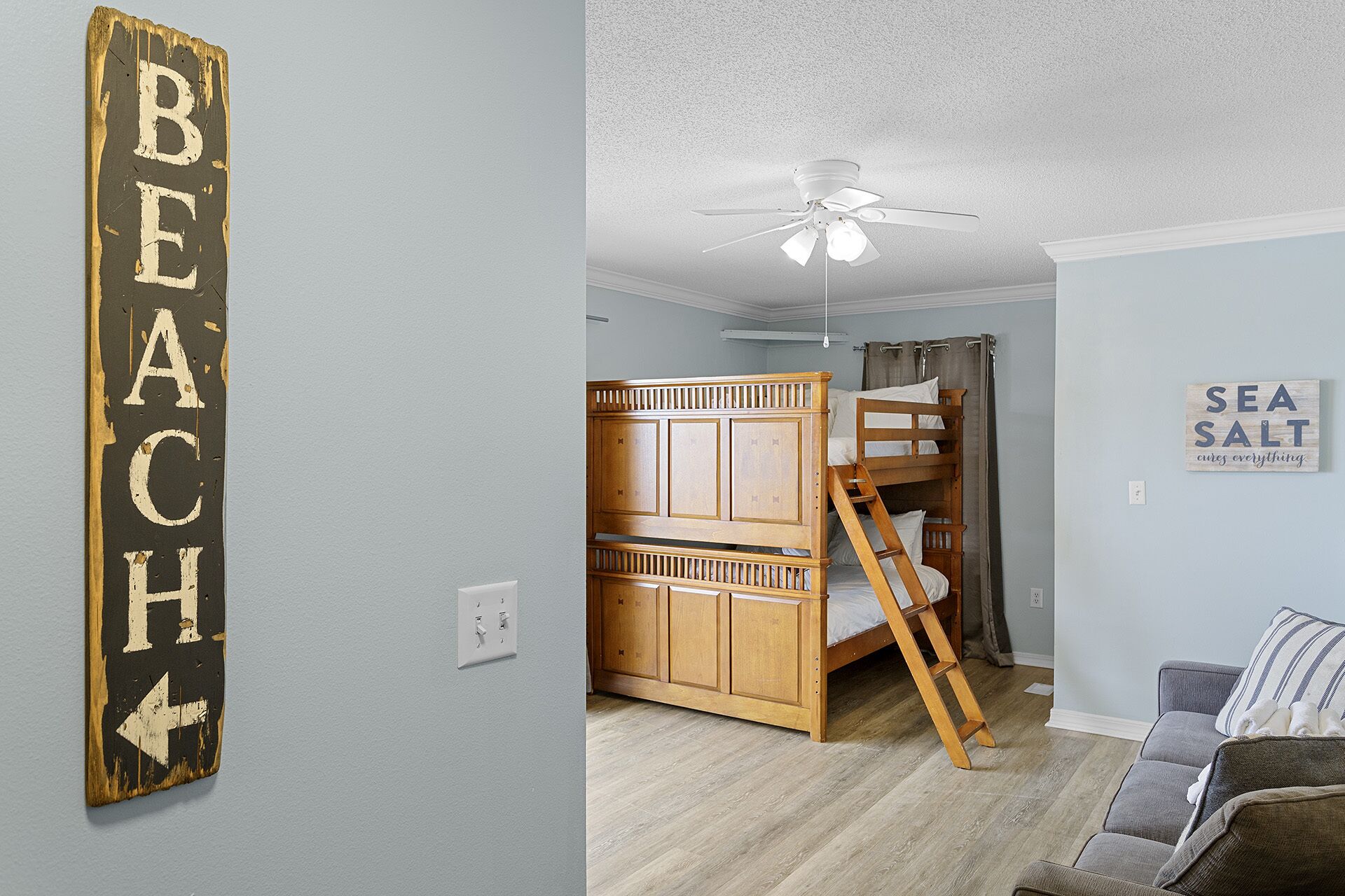 A room with a bunk bed, a ceiling fan, and a wall sign that reads "BEACH".