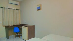 Habitació petita amb escriptori, cadira, llit i nevera de dimensions reduïdes.