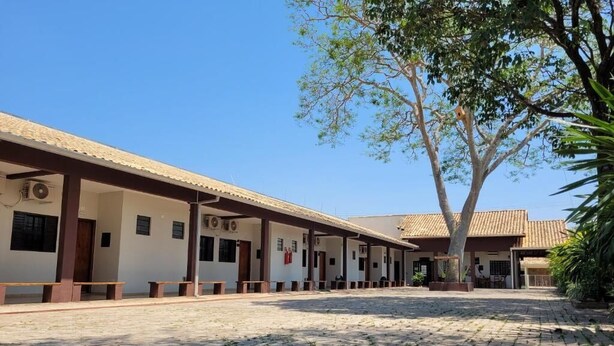 Un pati amb paviment de rajoles, zones d'estar cobertes i un edifici amb diverses habitacions.