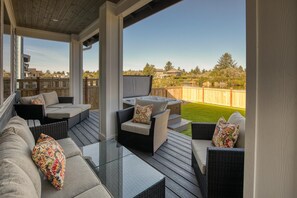 A covered outdoor patio with wicker furniture, a glass table, and a hot tub. - The Bridge House - Oyhut Bay Seaside Village (Ocean Shores)