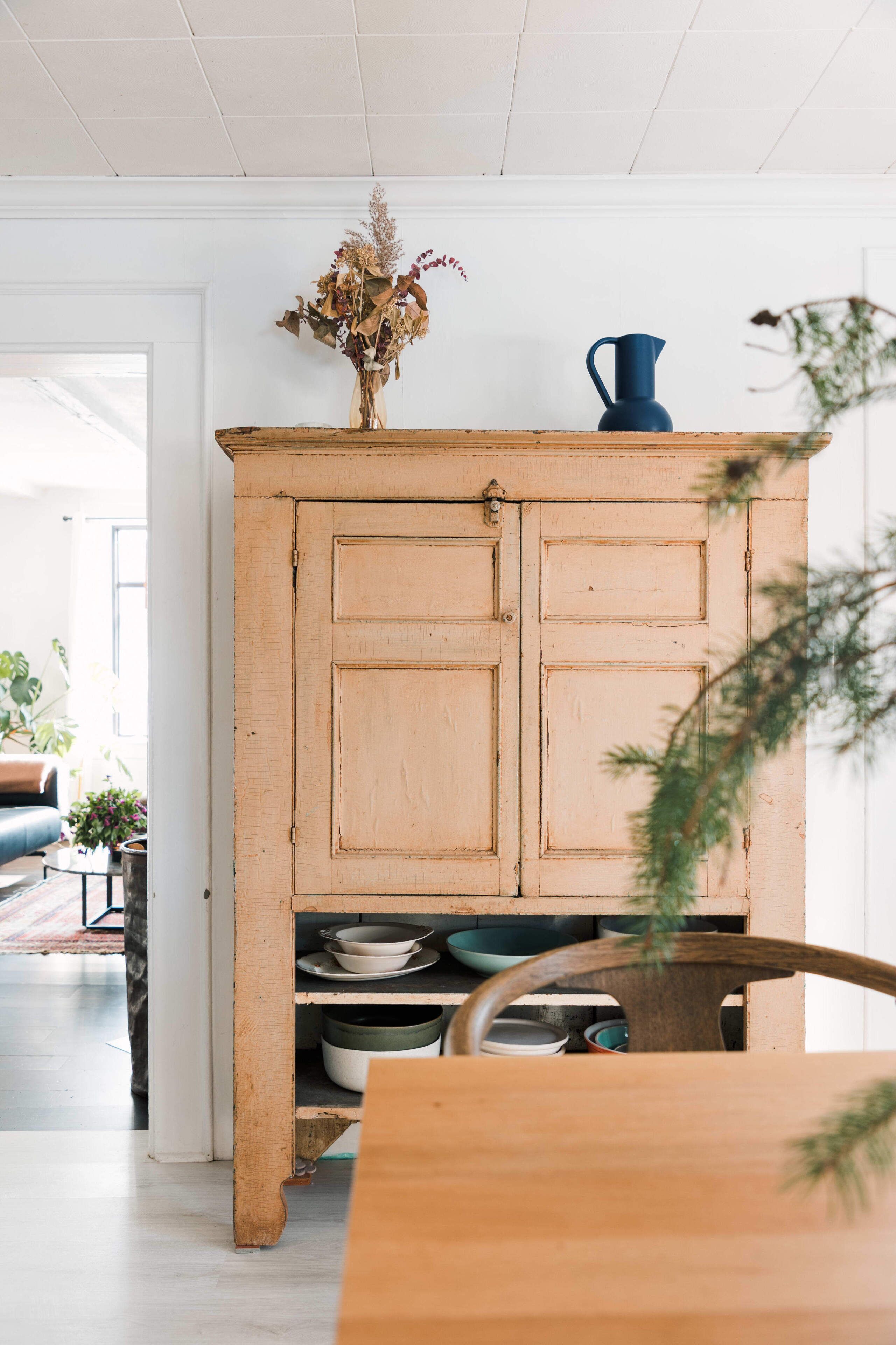 Un mueble de madera rústico con repisas, un florero con flores secas y una jarra azul.