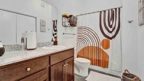 A bathroom with a double sink vanity, a toilet, and a shower curtain with abstract patterns.