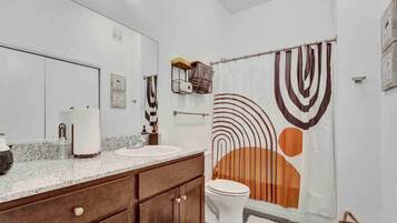 A bathroom with a double sink vanity, a toilet, and a shower curtain with abstract patterns.