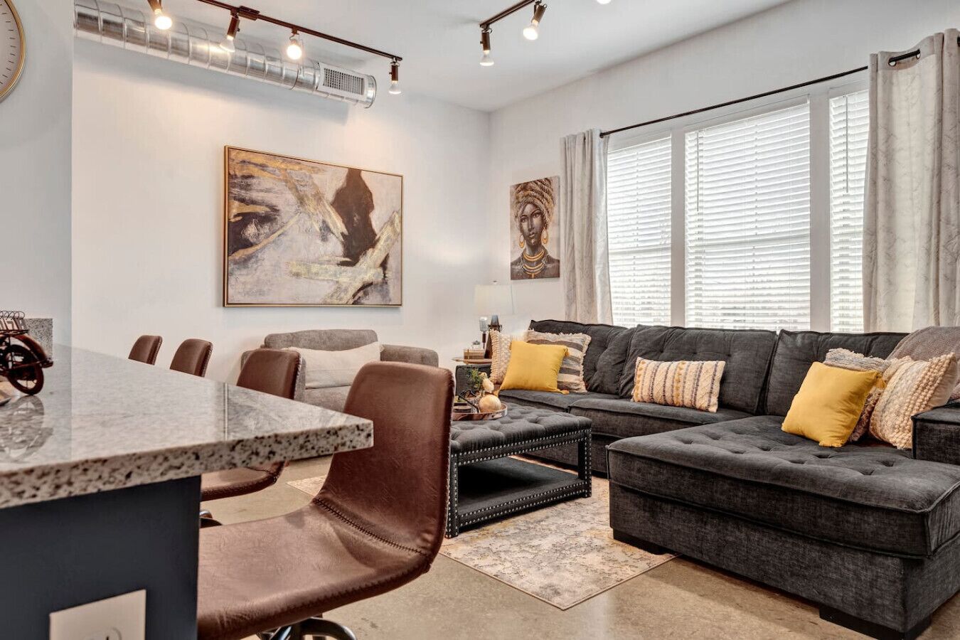 A modern living room with a dark grey sectional sofa, a round coffee table, and a dining area with a marble table and chairs.