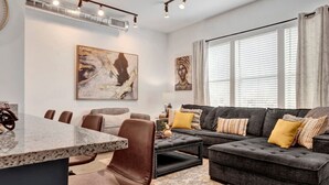 A modern living room with a dark grey sectional sofa, a round coffee table, and a dining area with a marble table and chairs.