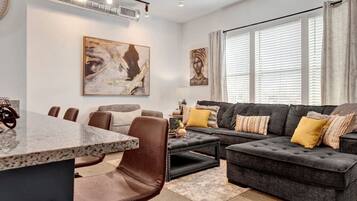 A modern living room with a dark grey sectional sofa, a round coffee table, and a dining area with a marble table and chairs.