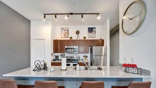 A modern kitchen with granite countertops, stainless steel appliances, and a large wall clock.