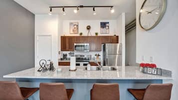 A modern kitchen with granite countertops, stainless steel appliances, and a large wall clock.