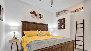 A bedroom with a wooden bed, a bedside table with a lamp, a ladder, and wall art.