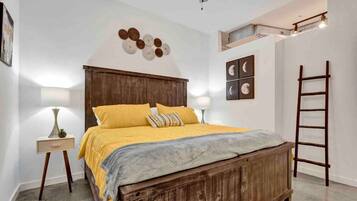 A bedroom with a wooden bed, a bedside table with a lamp, a ladder, and wall art.