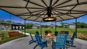 Une terrasse extérieure avec des fauteuils Adirondack bleus, un foyer et un espace abrité doté d’un toit en métal.