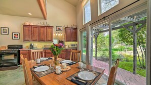 A dining area with a wooden table set for four, surrounded by wooden chairs. There is a large window providing a view of the outdoors. - 'Hilltop Loft' Ukiah Vacation Rental! (Ukiah)
