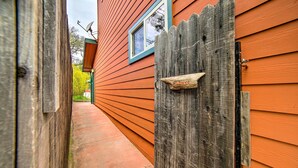 A narrow pathway leading to a wooden gate with an 'Entrance' sign, flanked by wooden siding and a window with a blue frame. - 'Hilltop Loft' Ukiah Vacation Rental! (Ukiah)