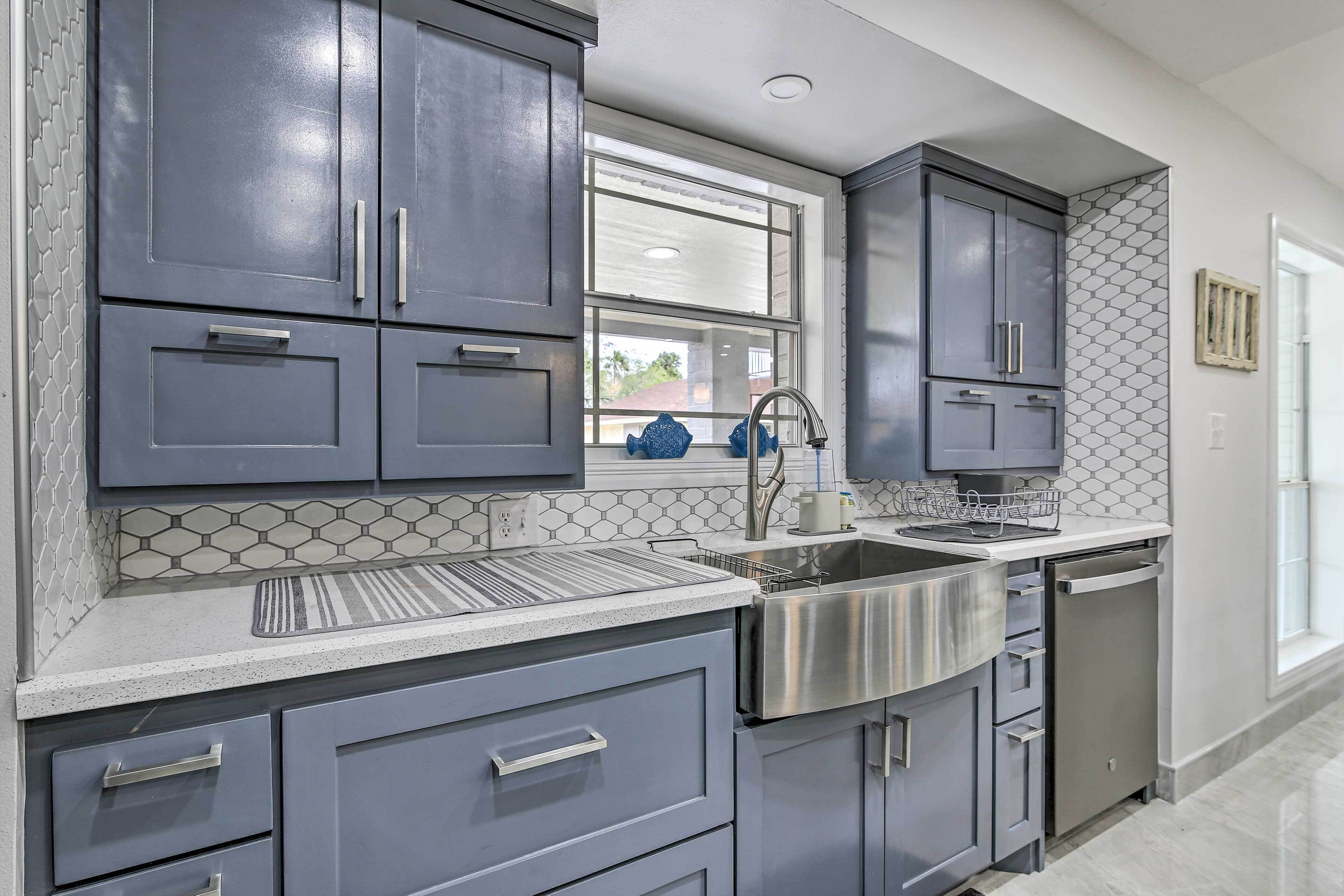 A modern kitchen with grey cabinets, stainless steel appliances, and a hexagonal tile backsplash.
