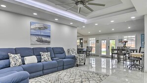 Ein modernes Wohnzimmer mit einem blauen Sofa, gemusterten Sessel, einer Essecke mit Tisch und Stühlen sowie einem Deckenventilator.
