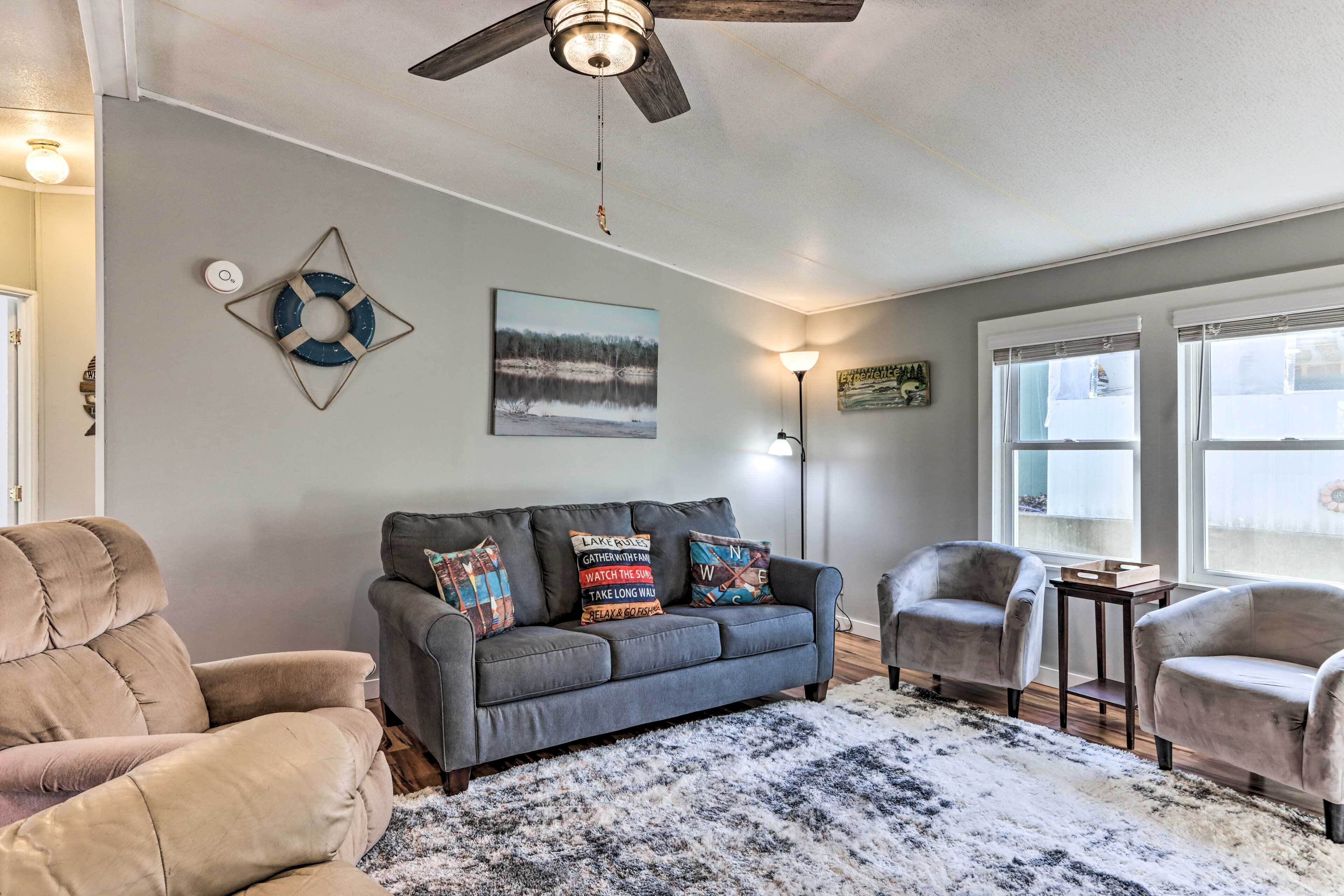 A living room with a gray sofa, two armchairs, a ceiling fan, a rug, and a painting on the wall.