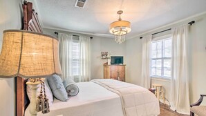 A bedroom with a large bed, a chandelier, a television, and a wooden cabinet. - Mississippi Cottage ~ 6 Mi to Columbus Lake (Columbus)