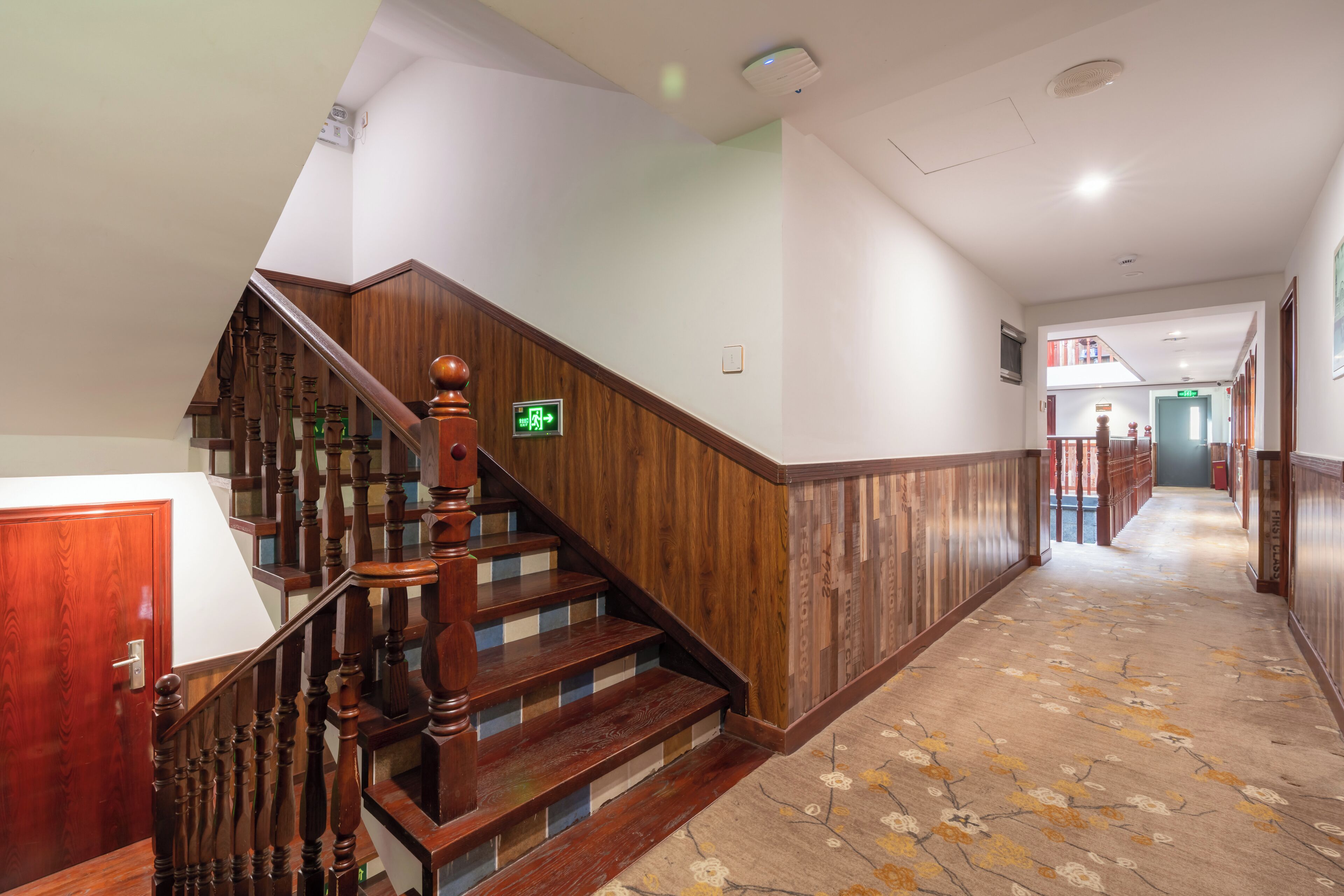 Un escalier en bois avec une rampe, un sol recouvert de moquette et une porte sur le côté gauche.