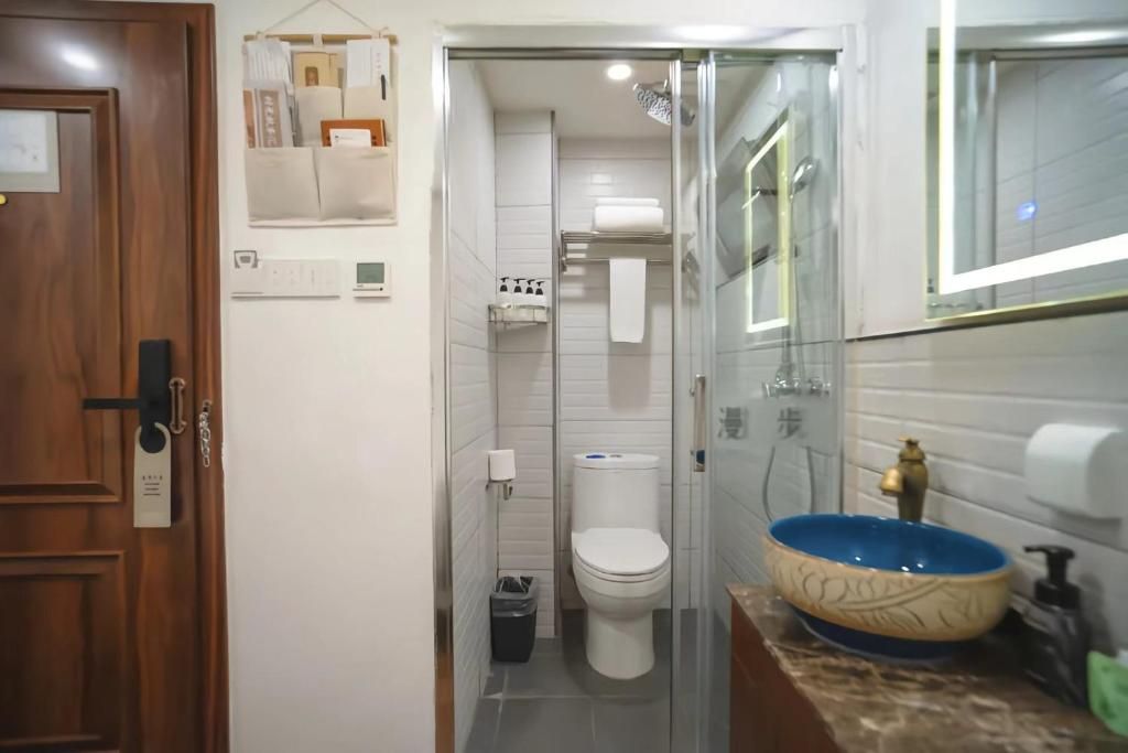A bathroom with a toilet, a glass shower enclosure, a sink with a blue basin, and a mirror above the sink.