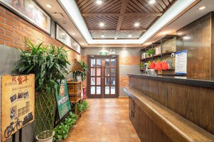 A reception area with a wooden reception desk, a brick wall with framed pictures, and a tiled floor.