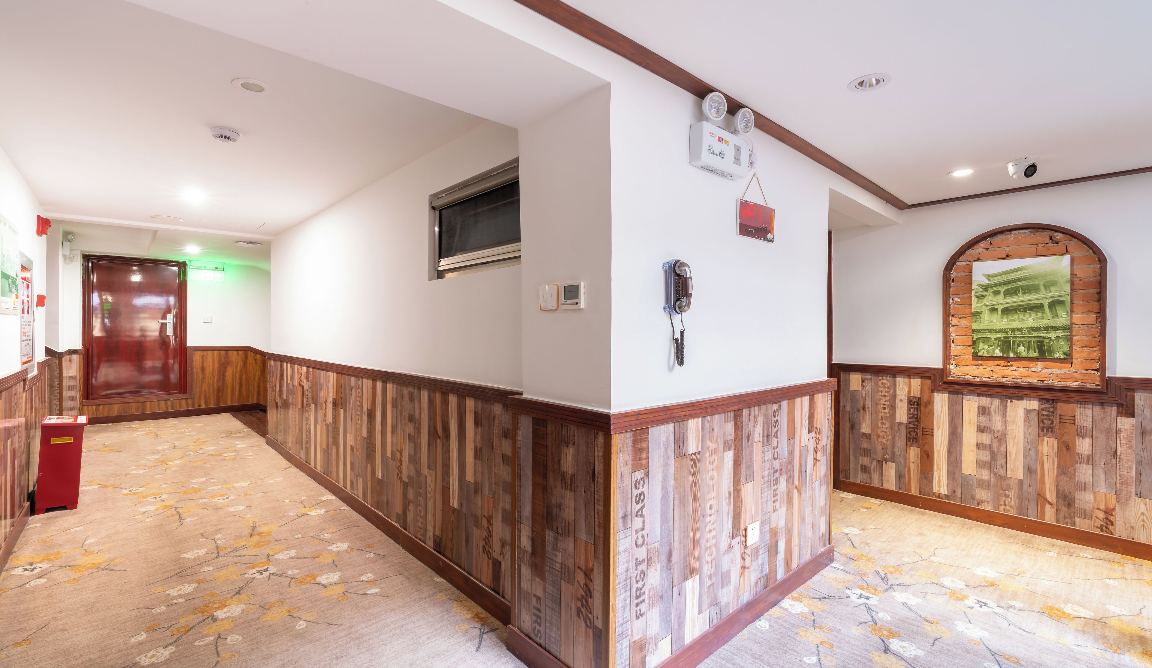 A hotel hallway with a wooden wainscoting, a telephone, and a wall-mounted picture frame.