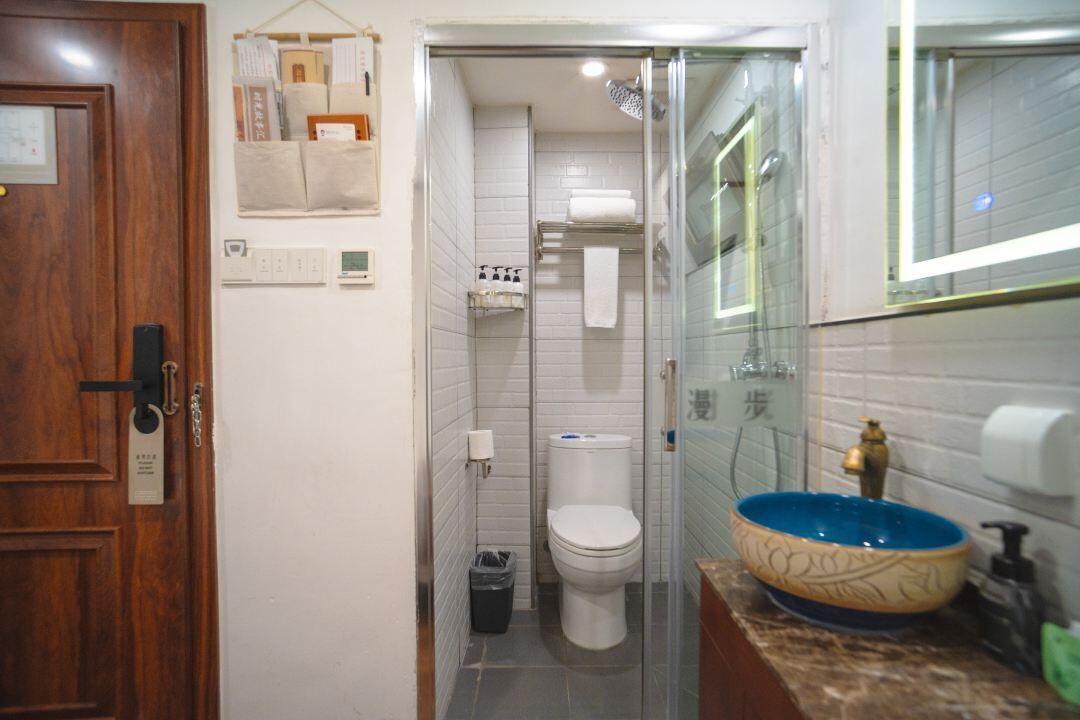 Un baño con inodoro, lavabo de color azul, ducha y puerta de madera.