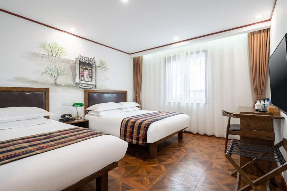 A hotel room with two beds, a desk, a TV, and a mural on the wall.