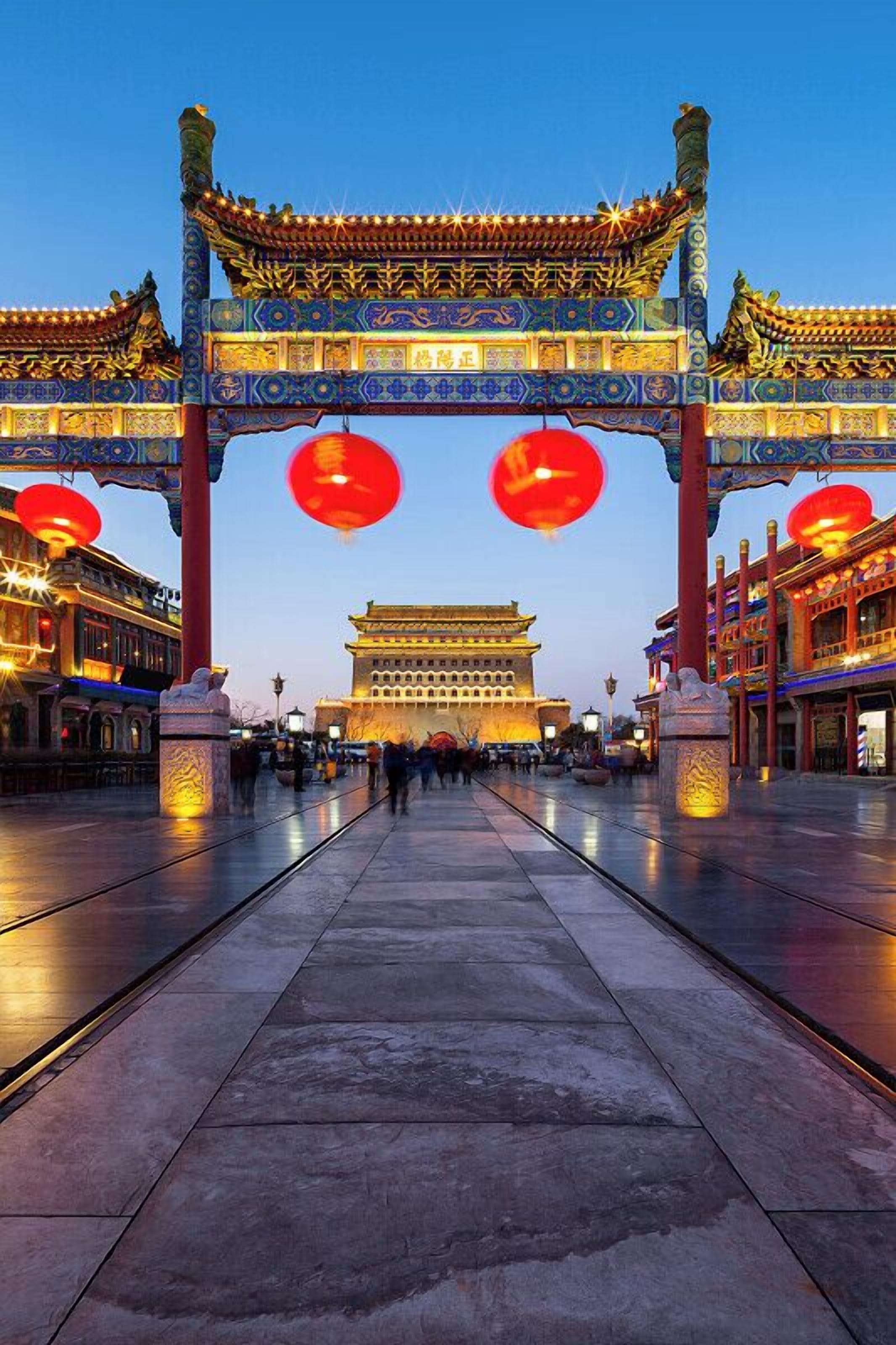 A traditional Chinese gate with intricate designs and red lanterns, leading to a historic building.