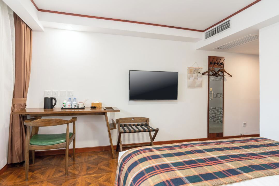 A hotel room with a bed, a desk with a chair, a television, and a wardrobe.