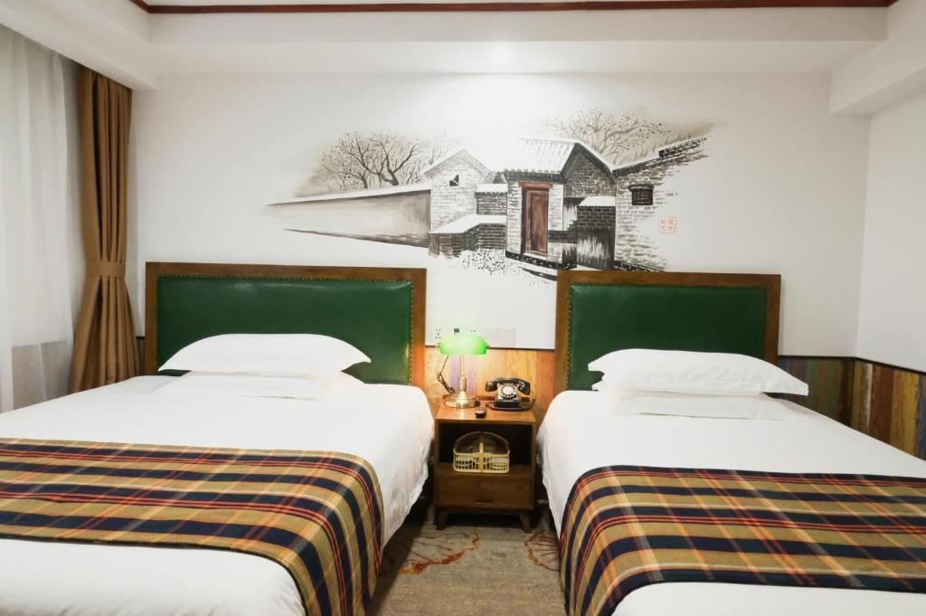 Una habitación de hotel con dos camas, una mesita de noche con lámpara y un cuadro en la pared.