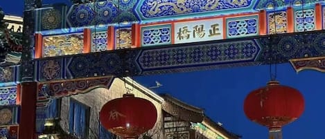 Une porte chinoise traditionnelle, ornée de motifs complexes aux couleurs bleu et or, de lanternes rouges et, en arrière-plan, d’un ciel d’un bleu limpide.