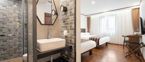 A hotel room with a shower, a sink, a bed, and a wooden floor.