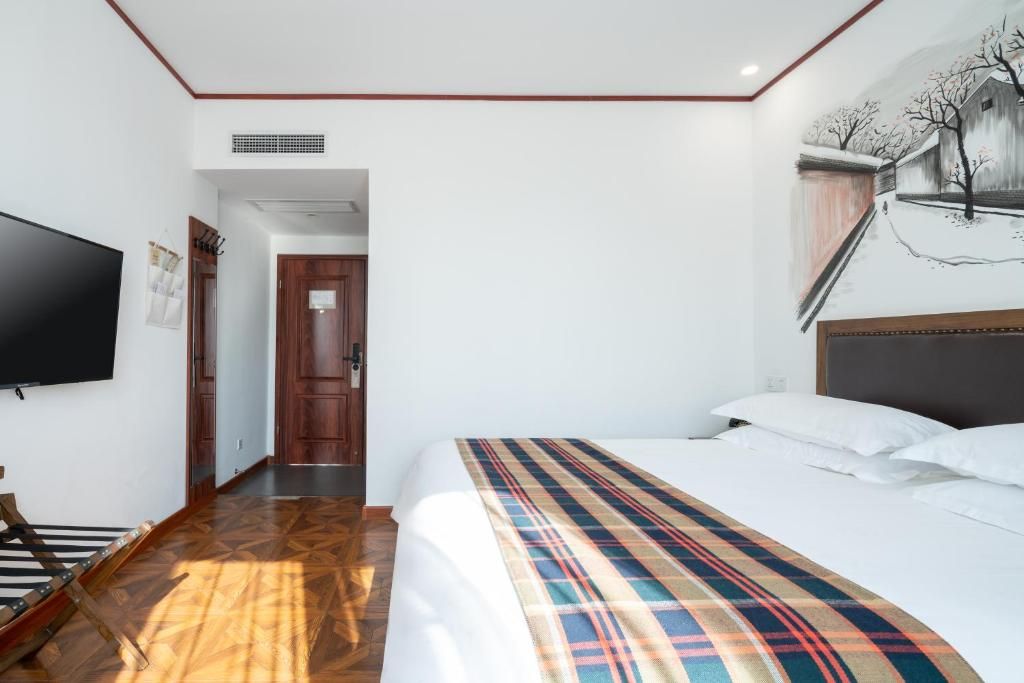 Una habitación de hotel con una cama, un televisor, piso de madera y una puerta que da a otra habitación.