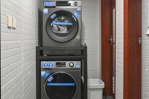 A compact laundry facility with two washers and dryers, a white trash bin, and a wooden door. - Nostalgia Hotel（Beijing Tiananmen Square ） (Beijing)