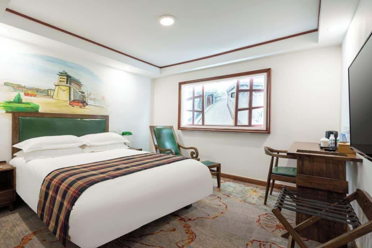A hotel room with a bed, a desk, a chair, a television, and artwork on the walls.