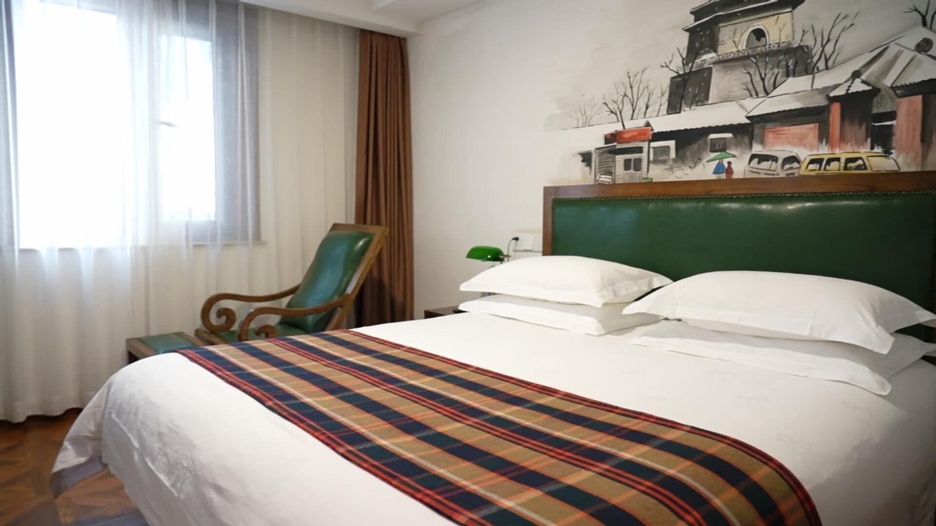 Habitación de hotel con cama, una silla, un cuadro en la pared y una ventana con cortinas.
