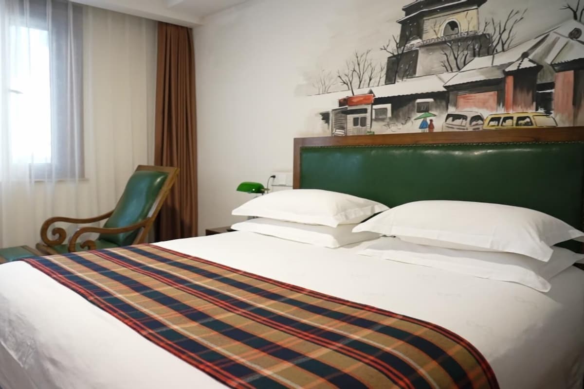 A hotel room with a bed, a chair, a painting on the wall, and a window with curtains.