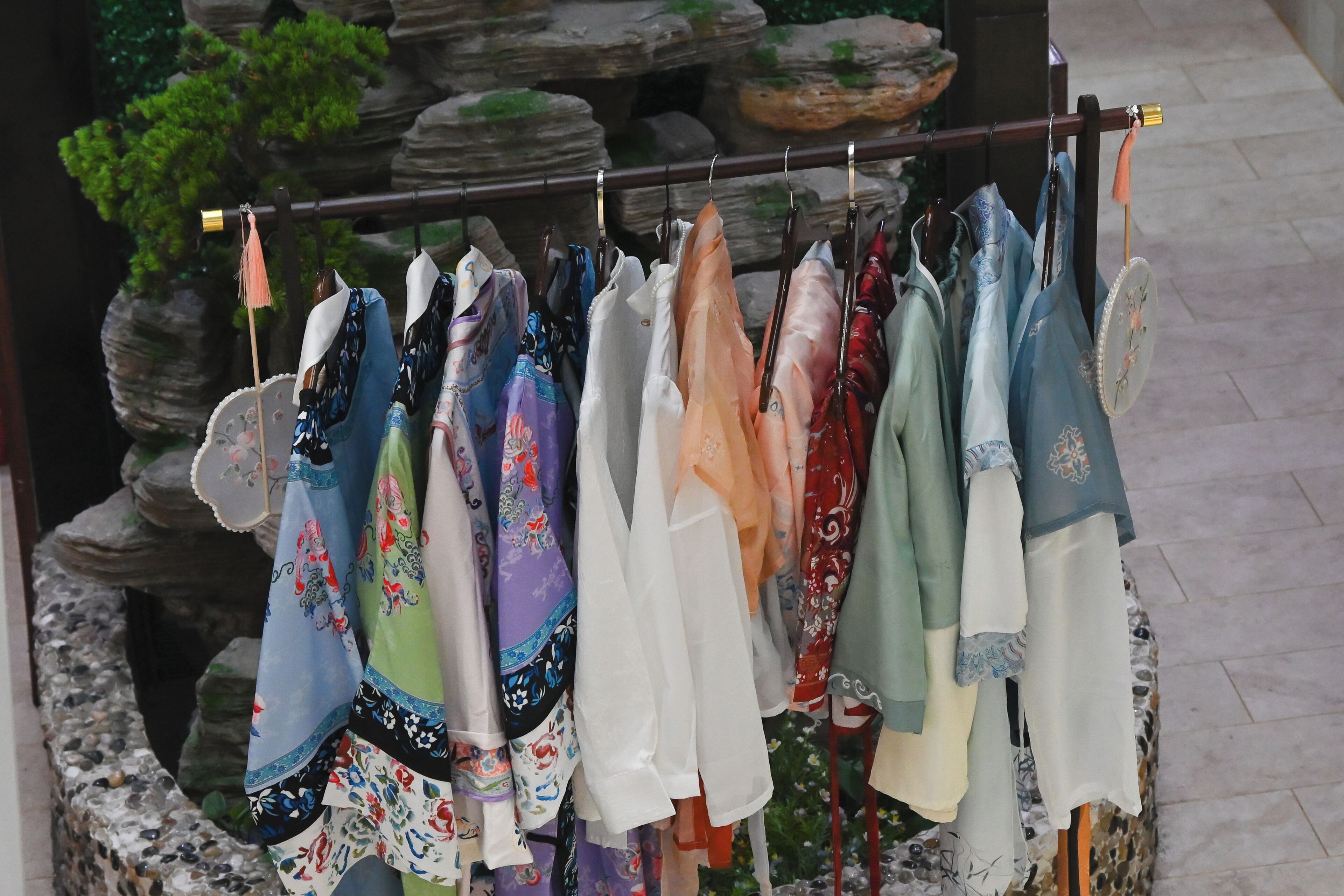 Un présentoir où sont suspendus divers foulards aux motifs variés, le tout installé en plein air, avec un paysage rocheux en arrière-plan.