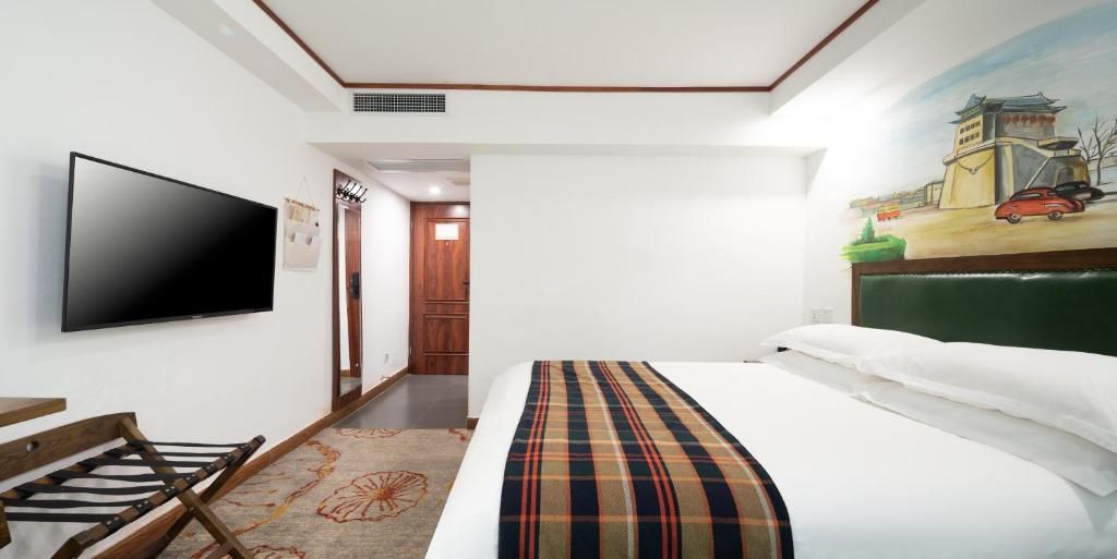 A hotel room with a bed, a television, a desk, and a painting on the wall.