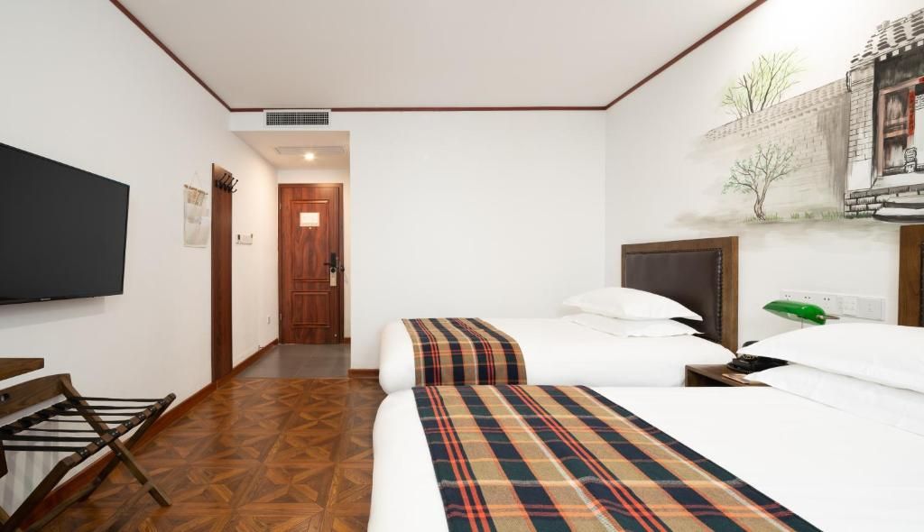 Habitación de hotel con dos camas, un televisor de pantalla plana, un banco de madera y un calentador fijado a la pared.