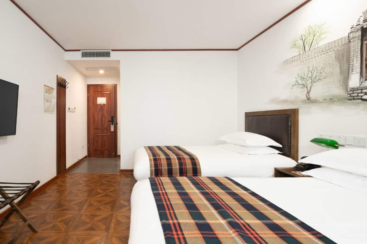 A hotel room with a bed, a TV, a wooden floor, and a door leading to another room.