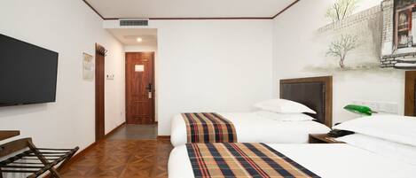 A hotel room with a bed, a TV, a wooden floor, and a door leading to another room.