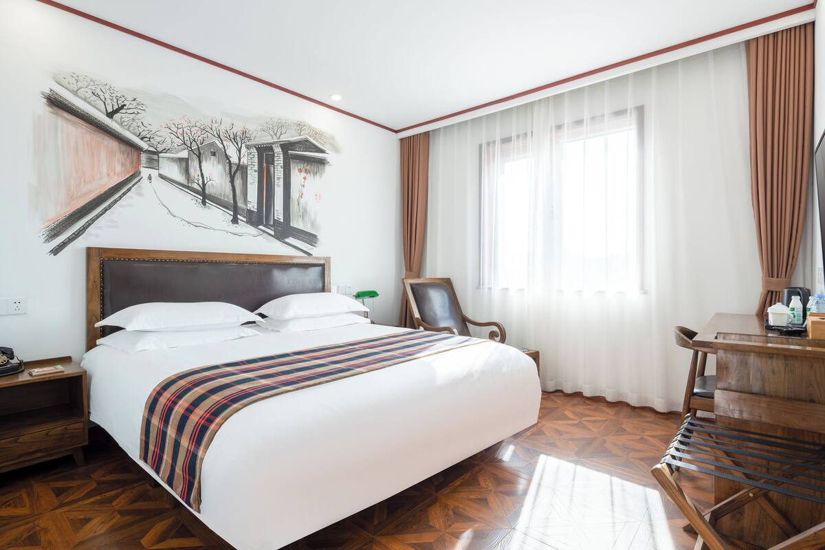 A hotel room with a large bed, a desk with a chair, a television, and a painting on the wall.