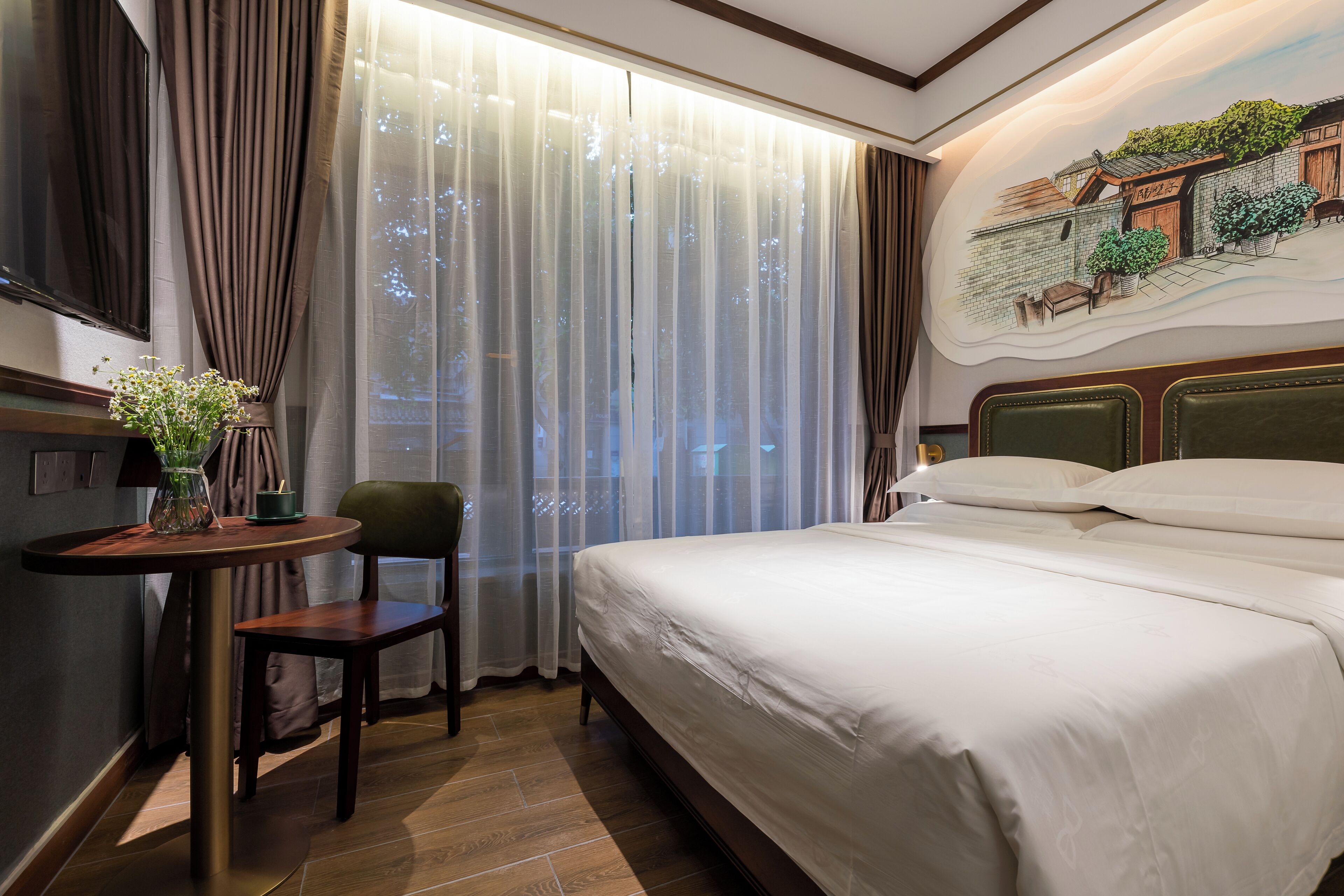 Un cuarto de hotel con una cama grande, una mesita con un florero, una silla y un cuadro en la pared.