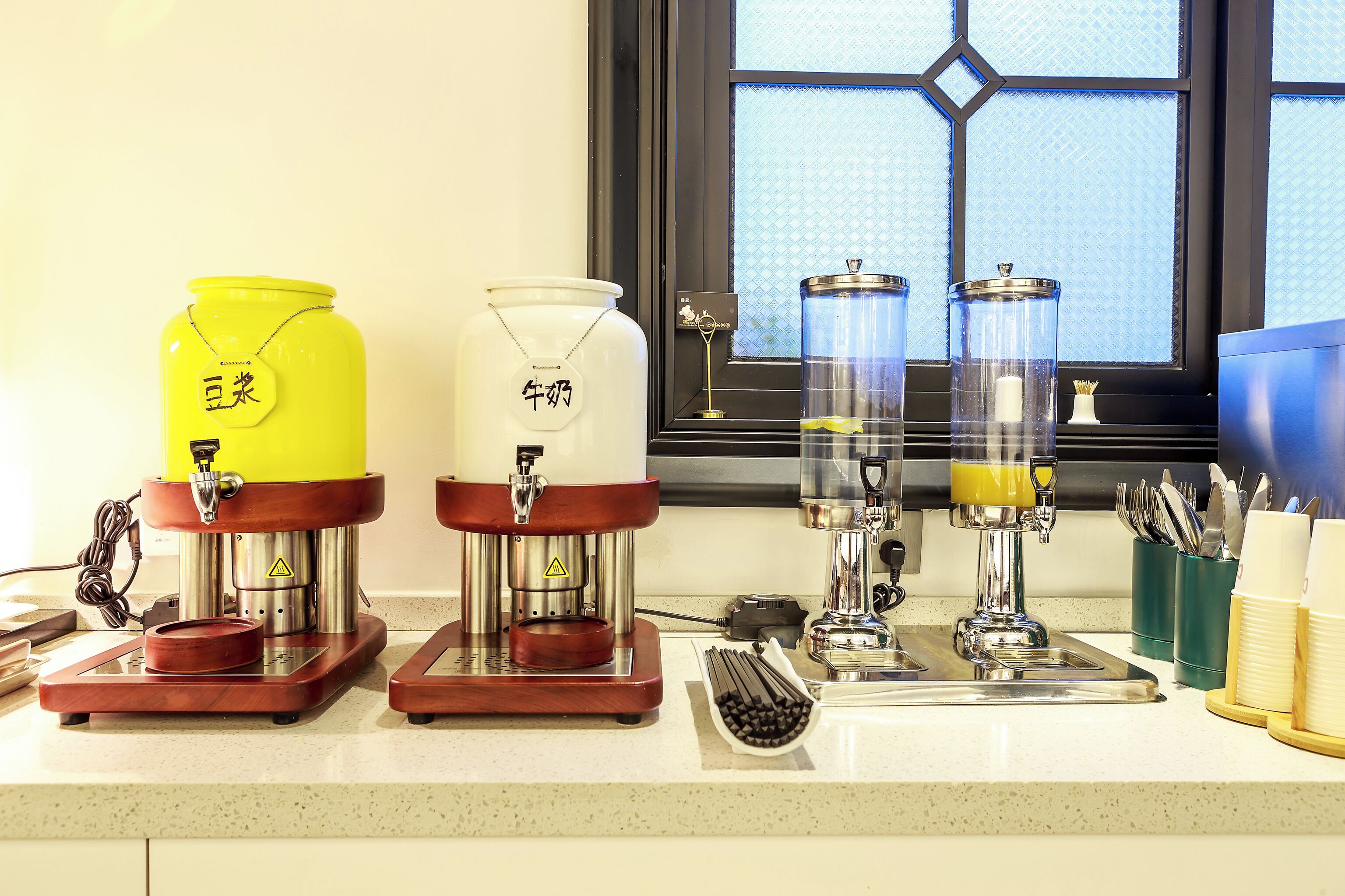 A kitchen counter with three coffee machines and a window with a view.