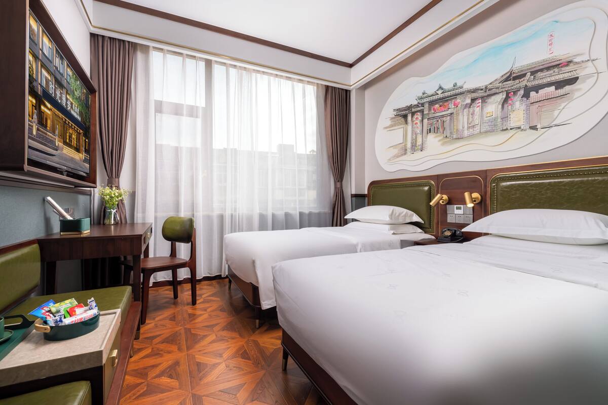 Une chambre d’hôtel avec deux lits, un bureau, une chaise et un grand tableau au mur.