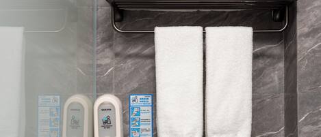 Une salle de bain avec deux serviettes blanches suspendues à un porte-serviettes, une paire de chaussons et un distributeur de gel hydroalcoolique.