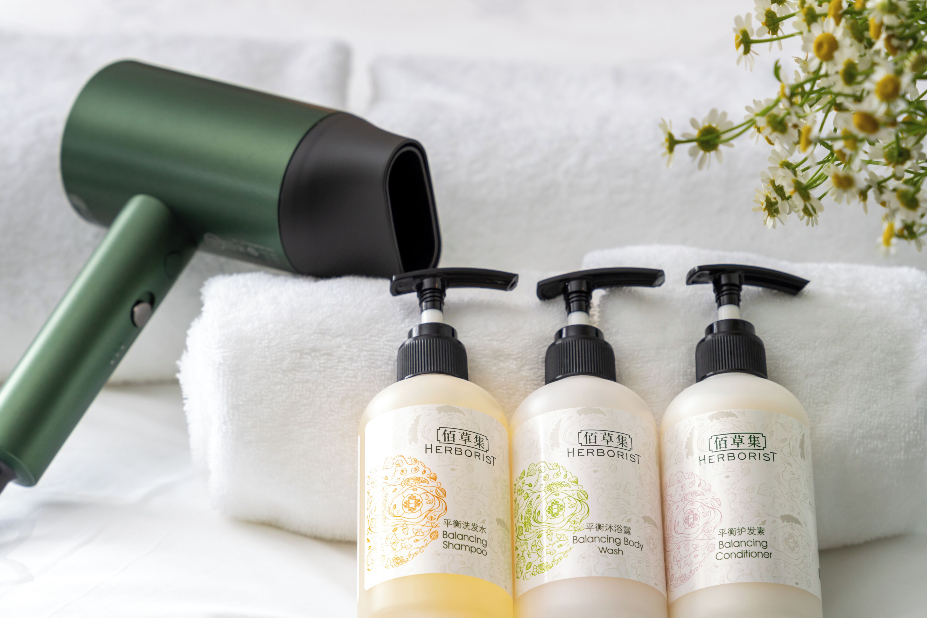 Un sèche-cheveux, trois flacons de gel douche et d’après-shampoing équilibrants, et une serviette blanche.
