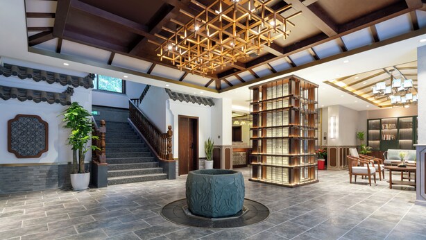 Een ruime lobby met een trap, een grote houten boekenkast en een decoratieve plantenbak in het midden.